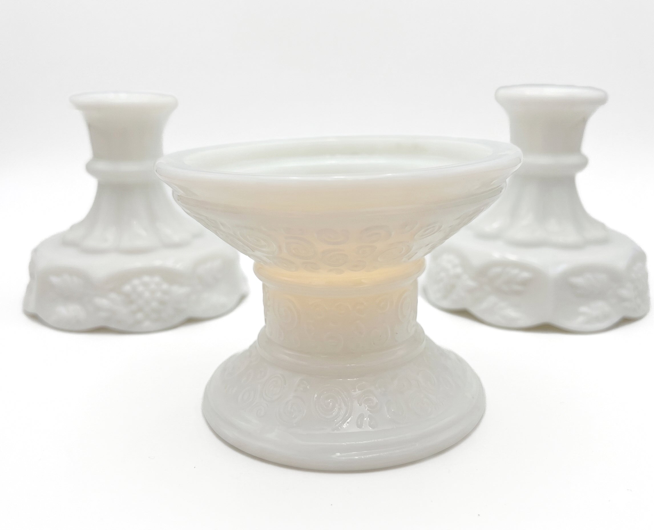 A curated trio of vintage milk glass candle holders in varying heights and classic patterns.